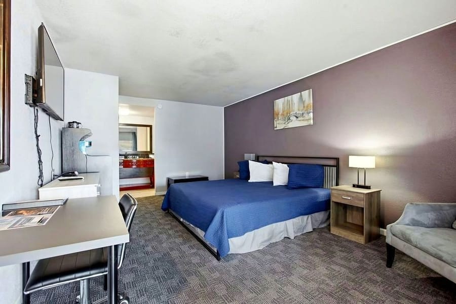 Deluxe King room with a blue bedspread, upholstered armchair and work desk