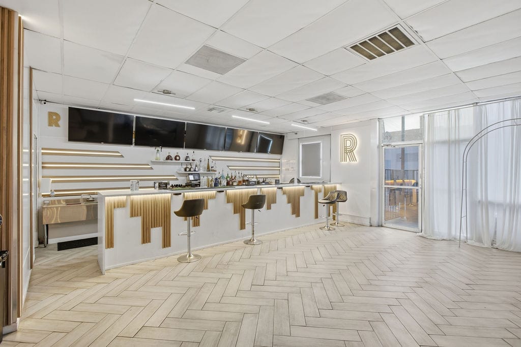 R Lounge bar with white and gold art-deco bar front, bar stools, and backlit shelving