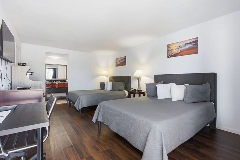 Deluxe Two Queen Beds Room with gray bedding, coastal artwork, and wood-style flooring