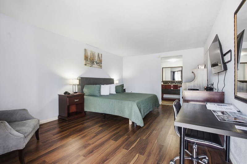 Deluxe King Room with sage green bedspread, wood-style flooring, nightstand, and armchair