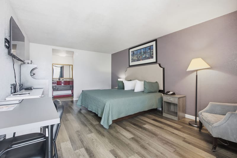 Deluxe King Room seen from the entrance with desk, TV, and floor lamp beside the bed