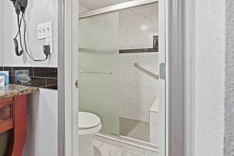 Renovated bathroom with tiled walk-in shower beside a granite-top vanity