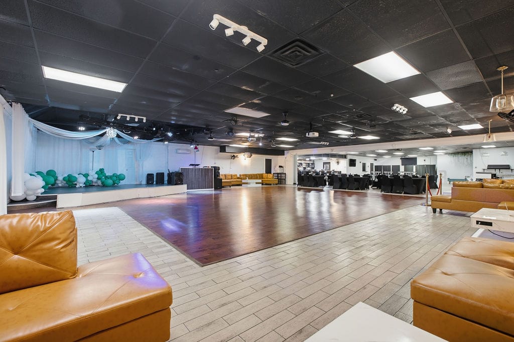Event hall with stage, balloon decor, dance floor, and draped backdrop
