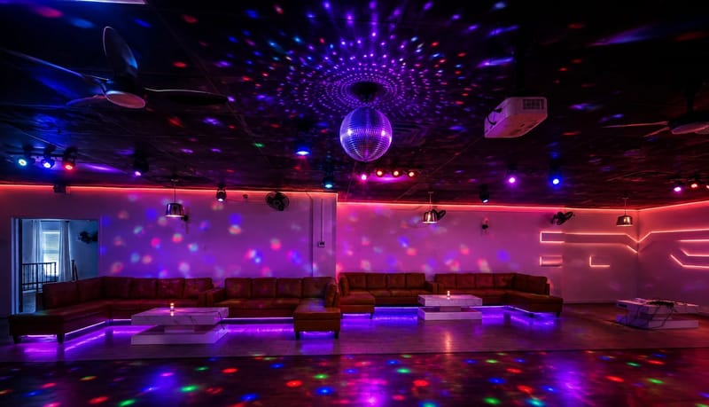 R Lounge in the evening with a mirror ball, colored lighting, and leather sectional seating