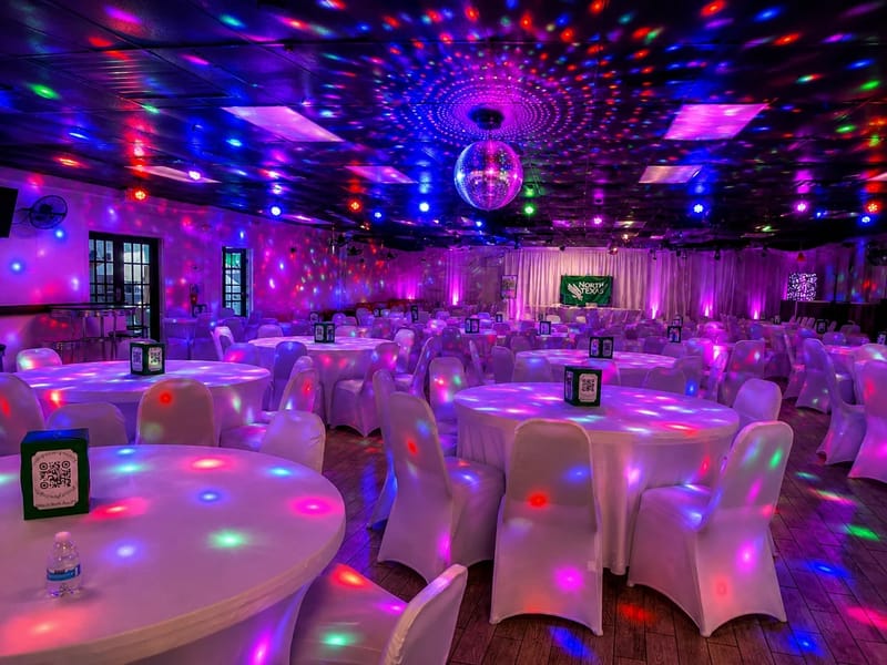 R Nite Star Event Center set for a banquet with round tables, white chair covers, and colored lighting