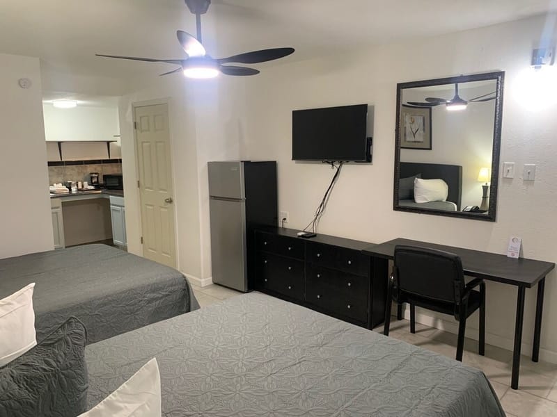 Studio Mini Kitchen 2 Queen with a ceiling fan, wall-mounted TV, dresser, desk, refrigerator, and the kitchenette beyond