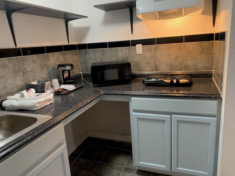 Kitchenette with a sink, microwave, two-burner cooktop, coffee maker, and white cabinets