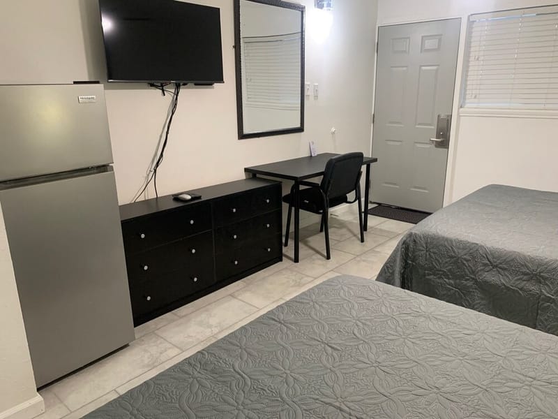 Full-height refrigerator, dresser, wall-mounted TV, and desk beside the two queen beds