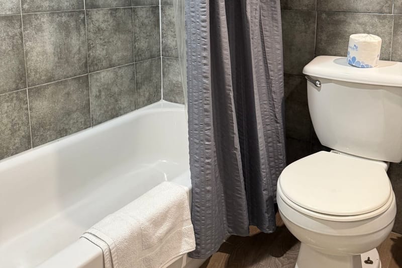Bathroom with a tub and shower, gray tile walls, and fresh towels