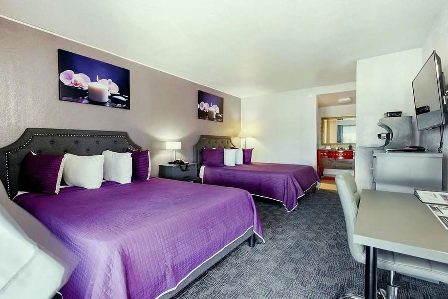 Premium room with two queen beds dressed in violet, beside a marble-top vanity